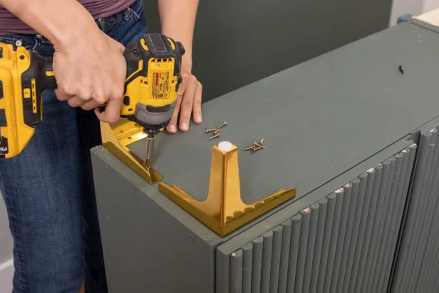 The next step in this DIY bold bar project is to screw brass legs to the bottom of the painted cabinets.